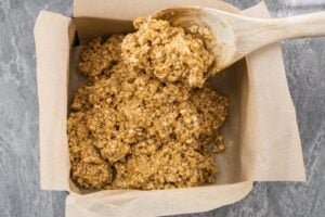 Scooping the oat flapjack mixture into a parchment paper lined cooking tin with a wooden spoon